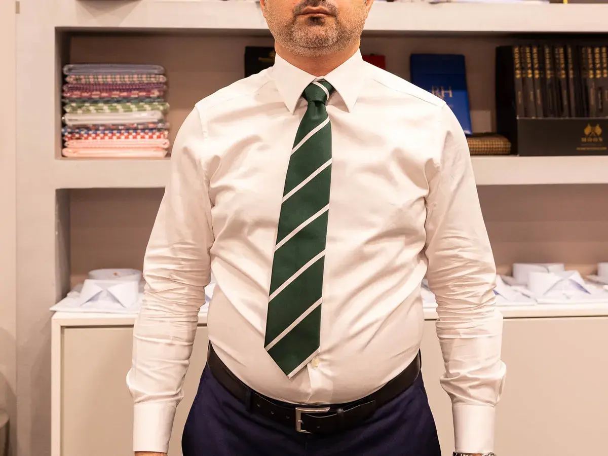 Uomo con camicia bianca e cravatta verde a righe, annodata con un elegante nodo mezzo windsor.