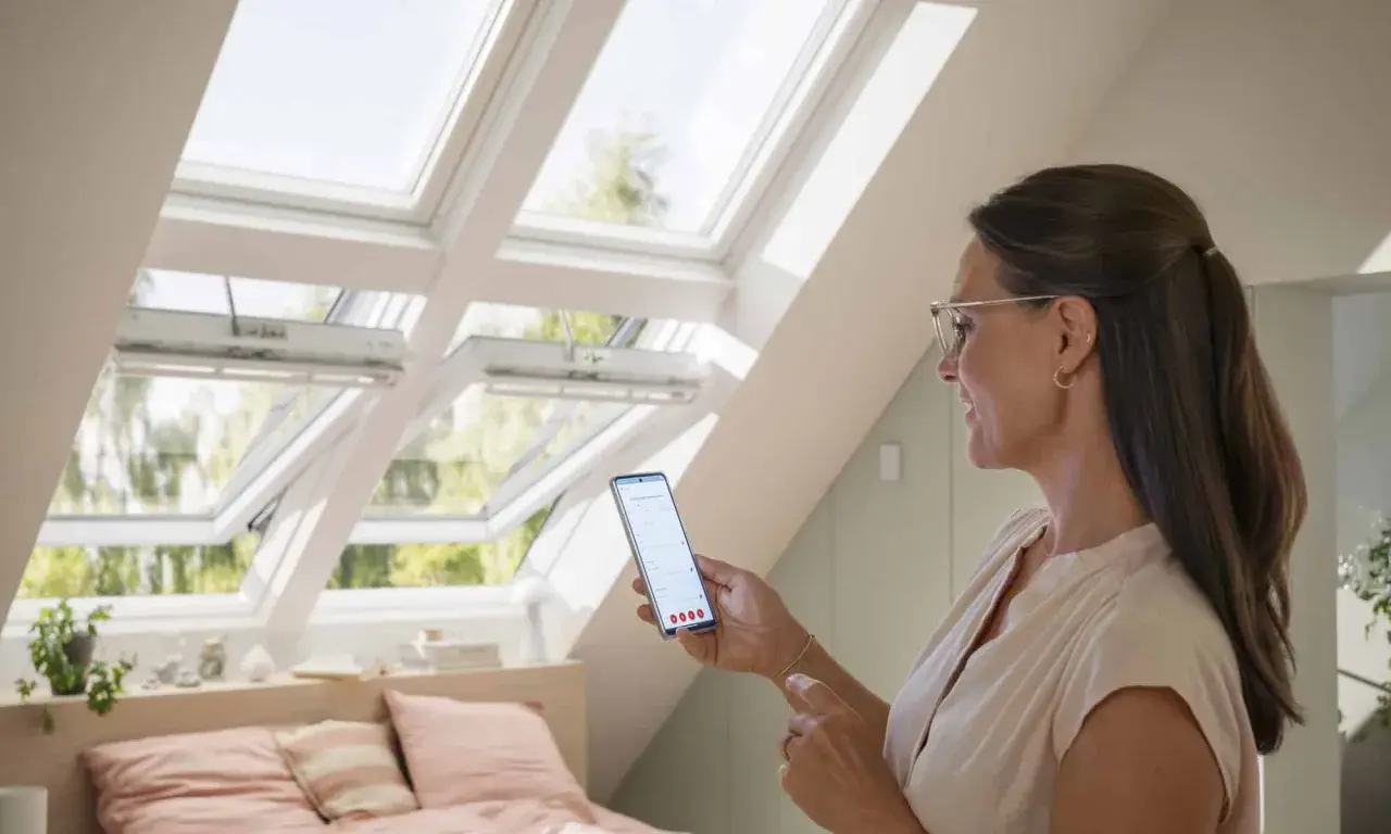 Une femme utilise son smartphone pour piloter des fenêtres de toit Velux.