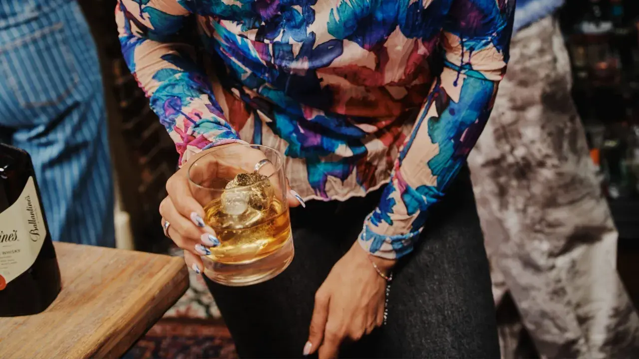 Kobieta trzyma szklankę z whisky Ballantine's. Zastanawia się, ile procent ma ten wyborny trunek.
