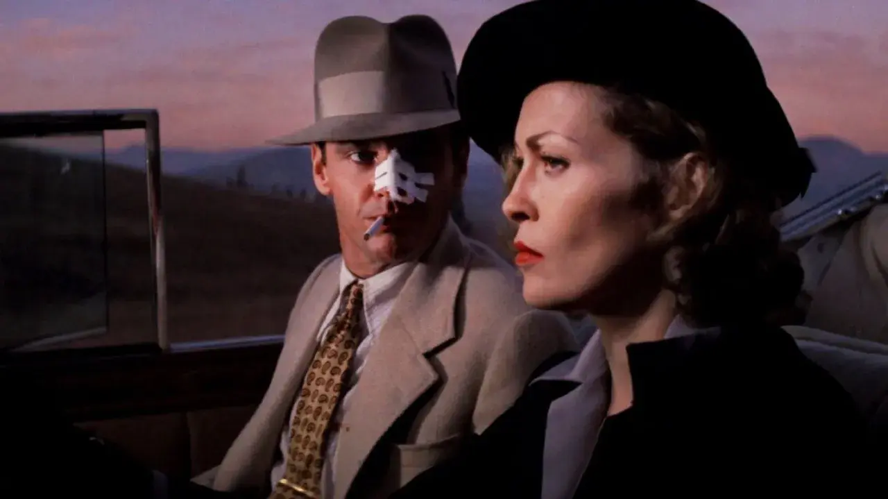 Jack Nicholson z plastrem na nosie i papierosem w ustach, obok Faye Dunaway w kapeluszu. Scena z jednego z filmów Romana Polańskiego.