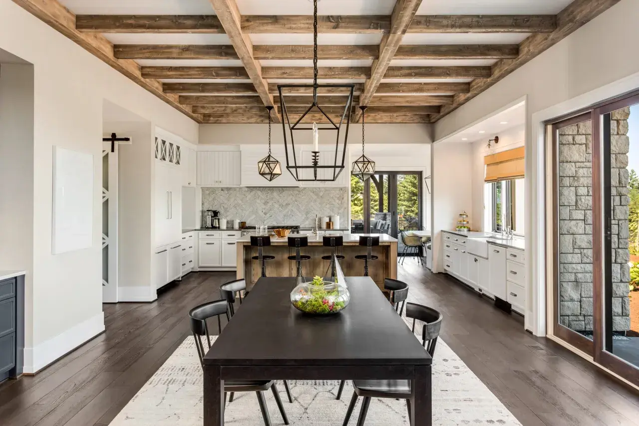 Comedor y cocina de estilo farmhouse con vigas de madera expuestas, isla central con taburetes y mesa oscura.