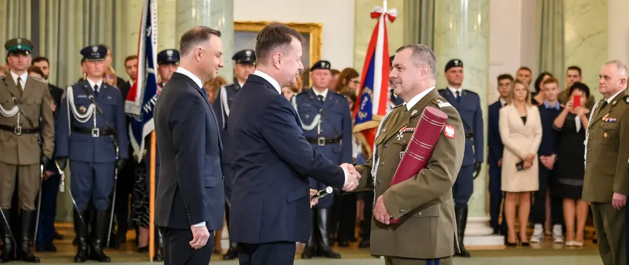 Uroczystość wręczenia nominacji generalskich. W centrum korpus generałów, prezydent Duda wręcza dokument.