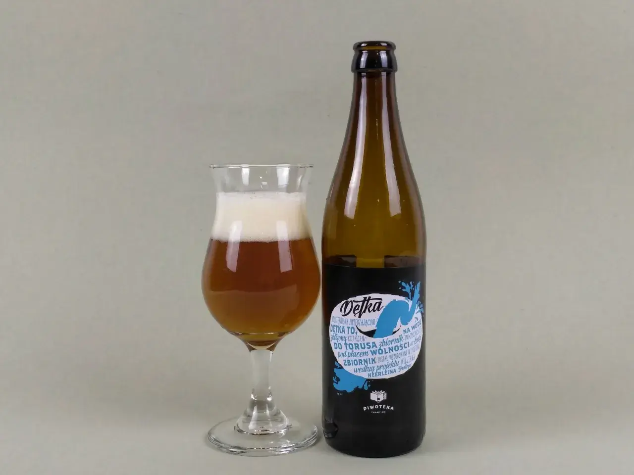 Szklanka z bursztynowym piwem i pianką obok butelki piwa typu new england ipa. Etykieta "Detka" z niebieskim motywem wodnym.