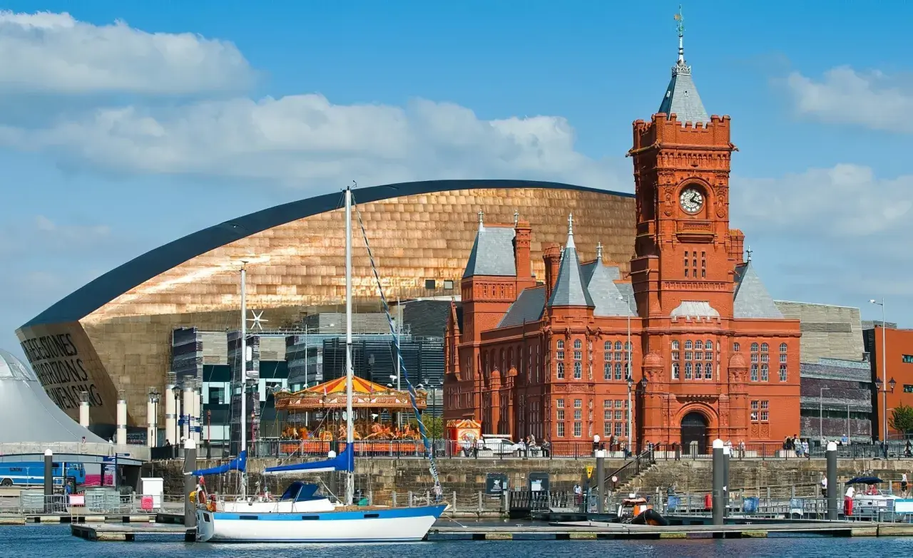 Bateaux amarrés dans le port de Cardiff, avec le bâtiment historique en brique rouge et le bâtiment moderne aux écailles cuivrées. Idéal pour visiter Cardiff.