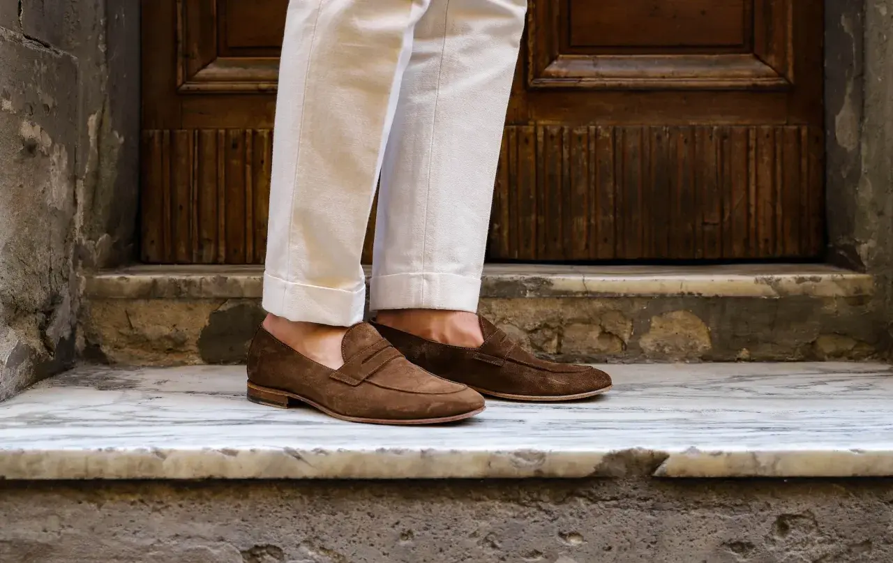 Pieds chaussés de mocassins marron en daim, un look estival parfait pour des chaussures sans chaussettes.