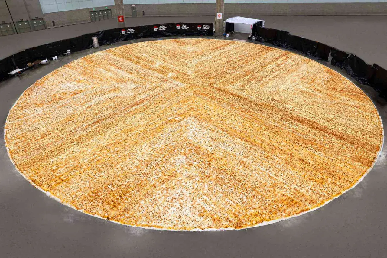 Gigantyczna pizza, największa na świecie, rozłożona na ogromnej przestrzeni. Jej złocisty kolor i równomierne posypanie przyprawami zachwycają.