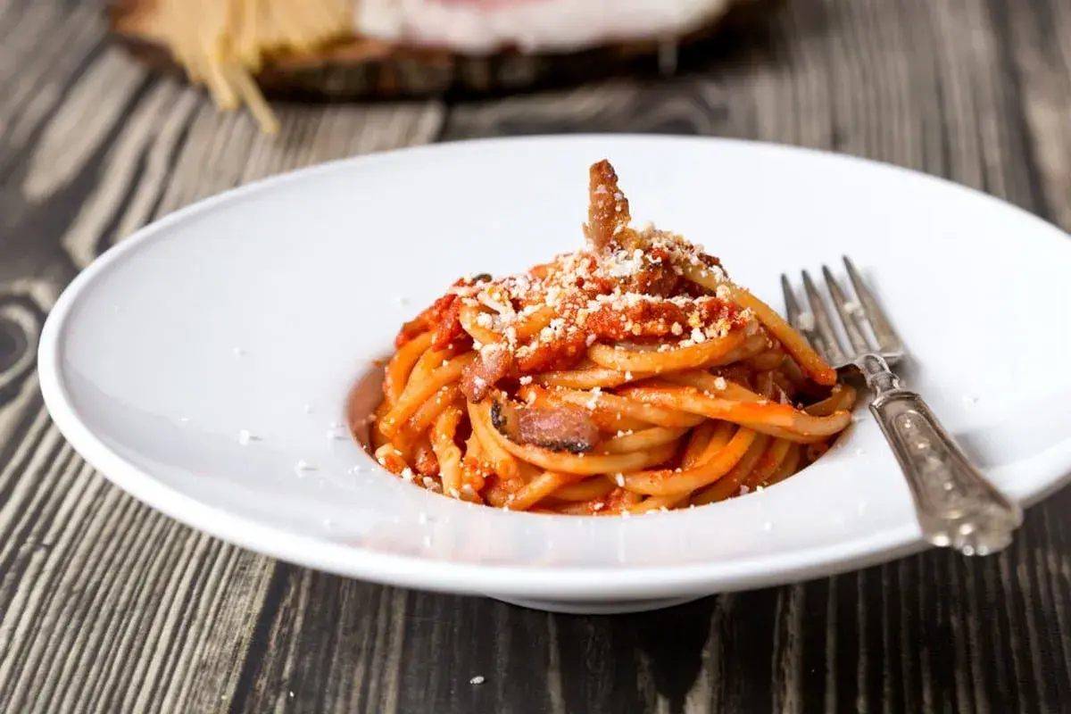 Un piatto di bucatini all'amatriciana, con guanciale croccante e una salsa rossa, spolverata di pecorino. La ricetta originale amatriciana cipolla, un classico intramontabile.