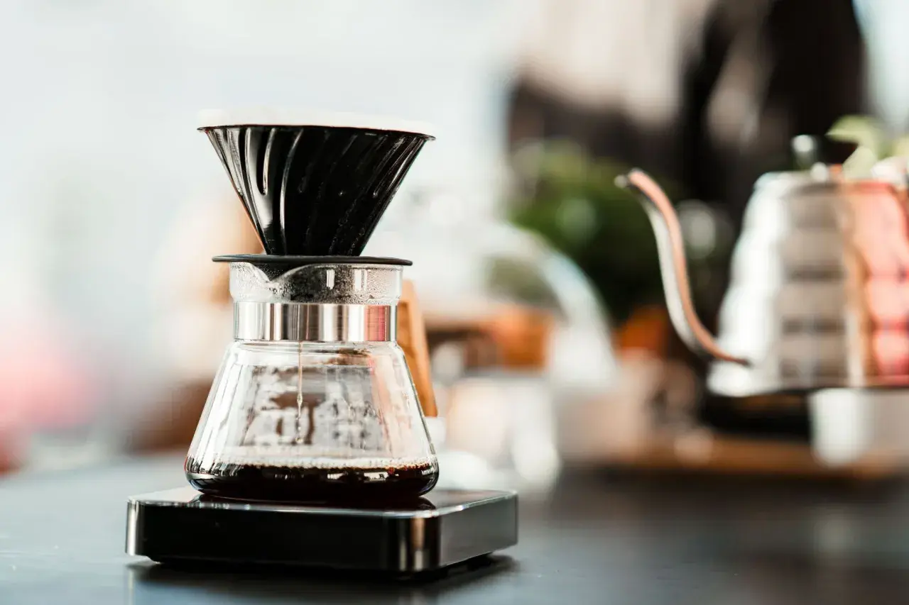 Kaffee tropft in eine Glaskaraffe, während sich der blooming effekt entfaltet. Im Hintergrund eine Kaffeekanne.