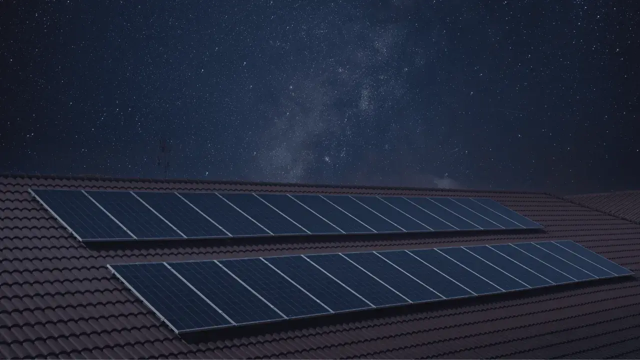 Paneles solares en un tejado bajo un cielo estrellado. La imagen sugiere que los paneles solares funcionan de noche, capturando la energía de las estrellas.