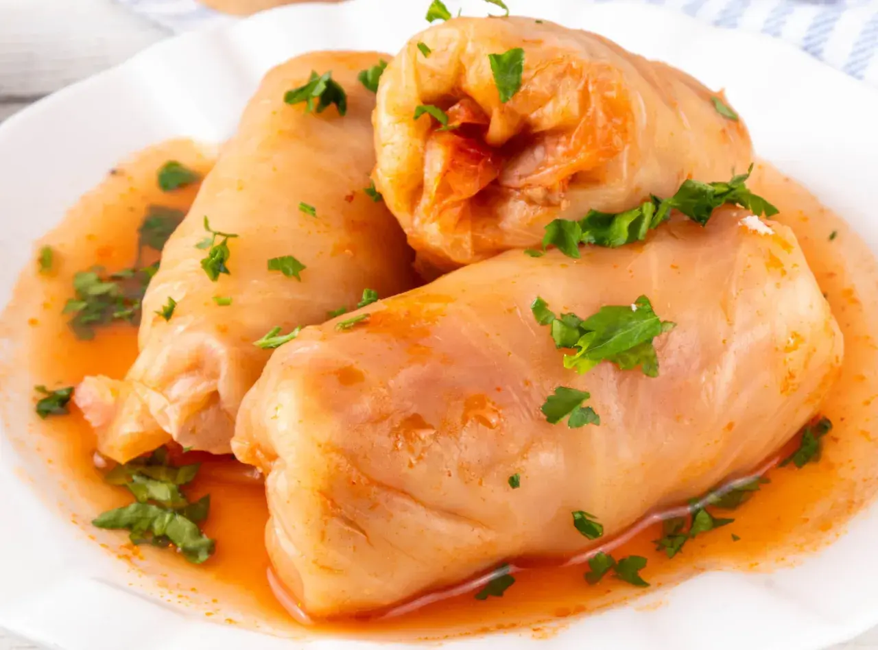 Gołąbki na 1kg mięsa, polane sosem pomidorowym i posypane natką pietruszki, gotowe do podania.