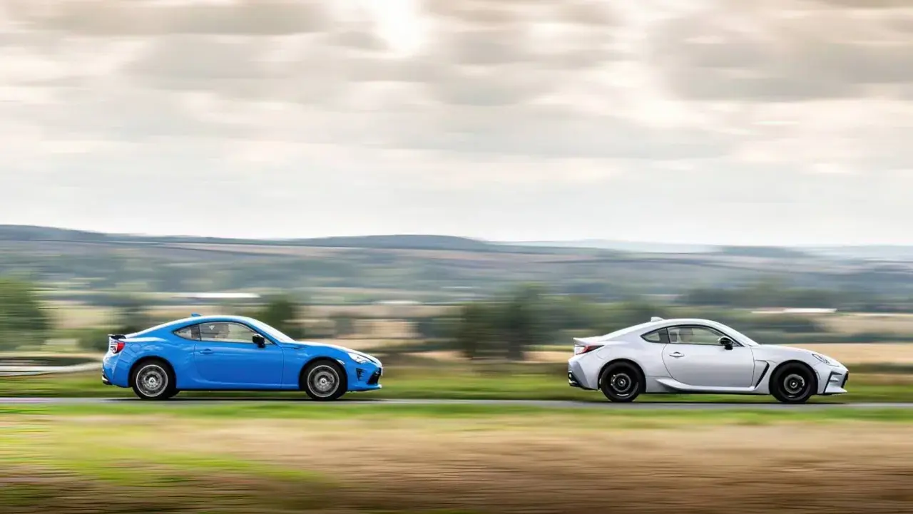 Dwa sportowe samochody, niebieska i srebrna Toyota 86, pędzą po wiejskiej drodze, tworząc dynamiczny obraz.