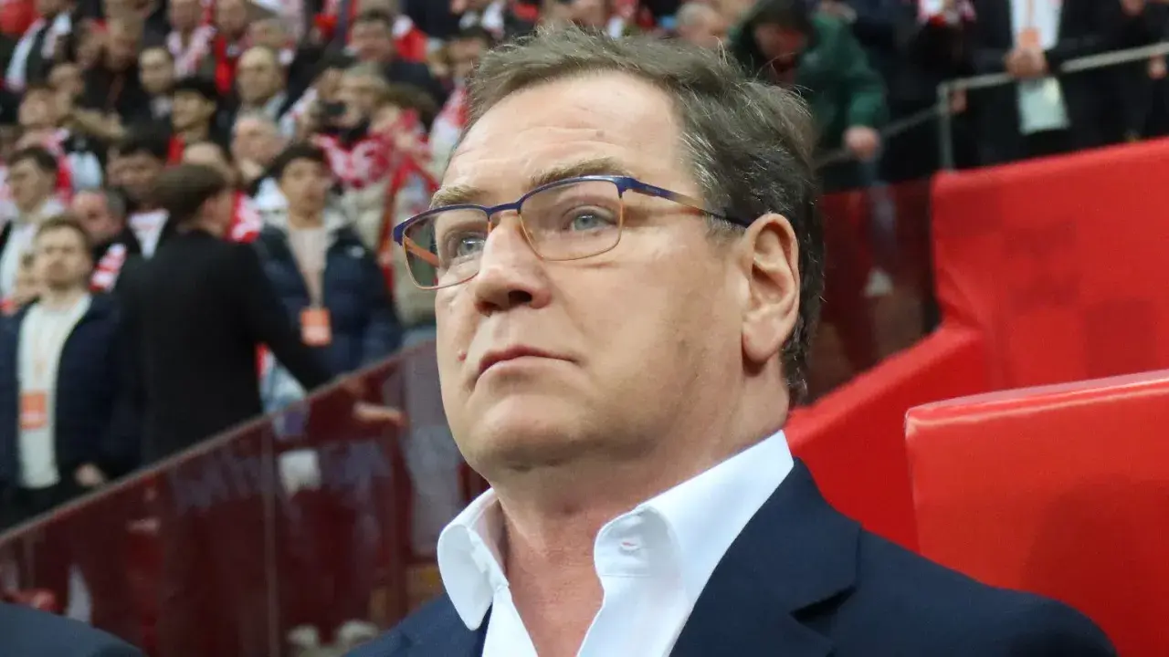 Trener w okularach z uwagą obserwuje trybuny, być może analizując potencjalnych kandydatów do reprezentacji.