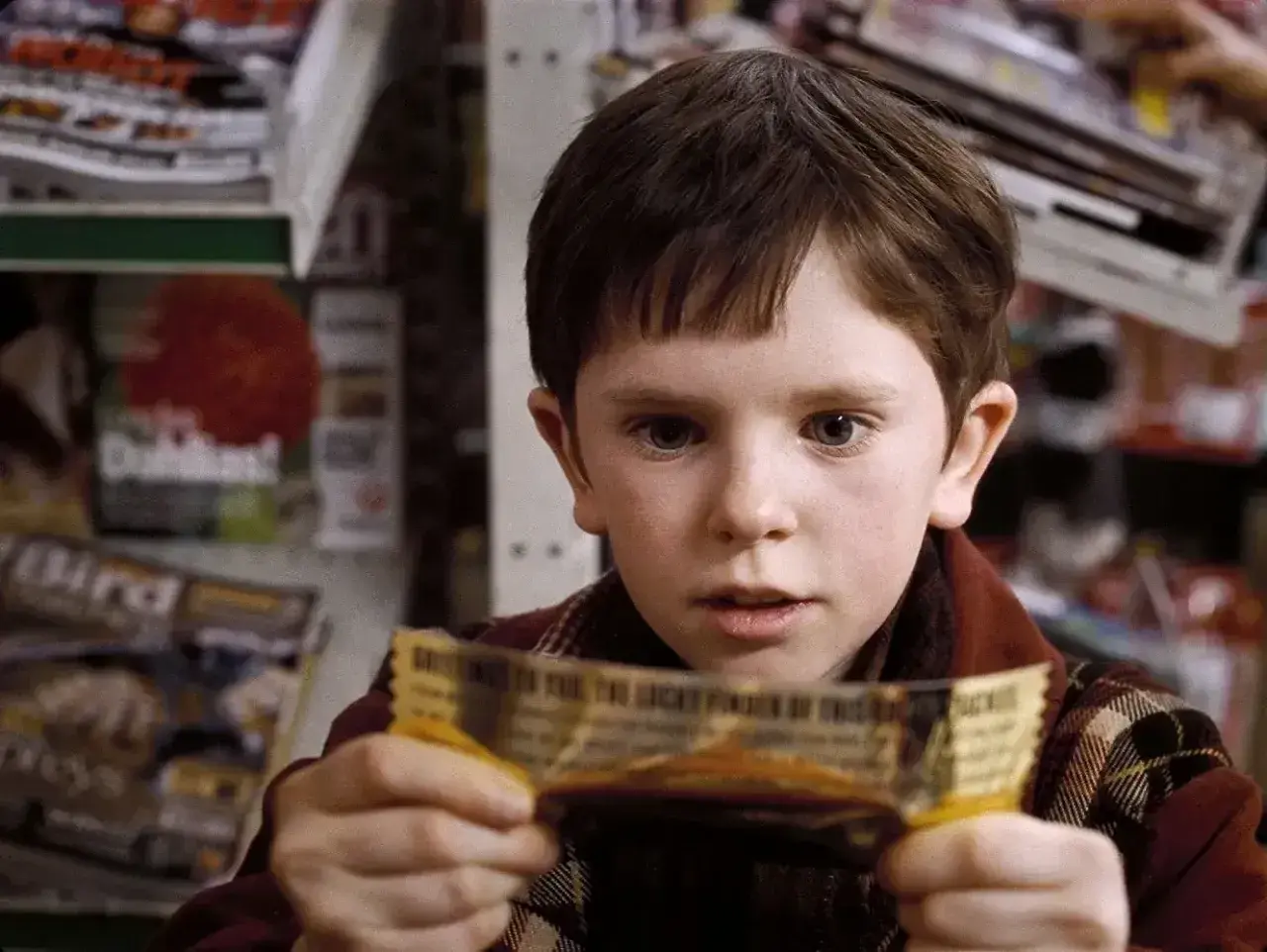 Chłopiec z filmu "Charlie i fabryka czekolady" trzyma złoty bilet. Freddie Highmore w tej roli to początek jego kariery w filmach, serialach i programach.