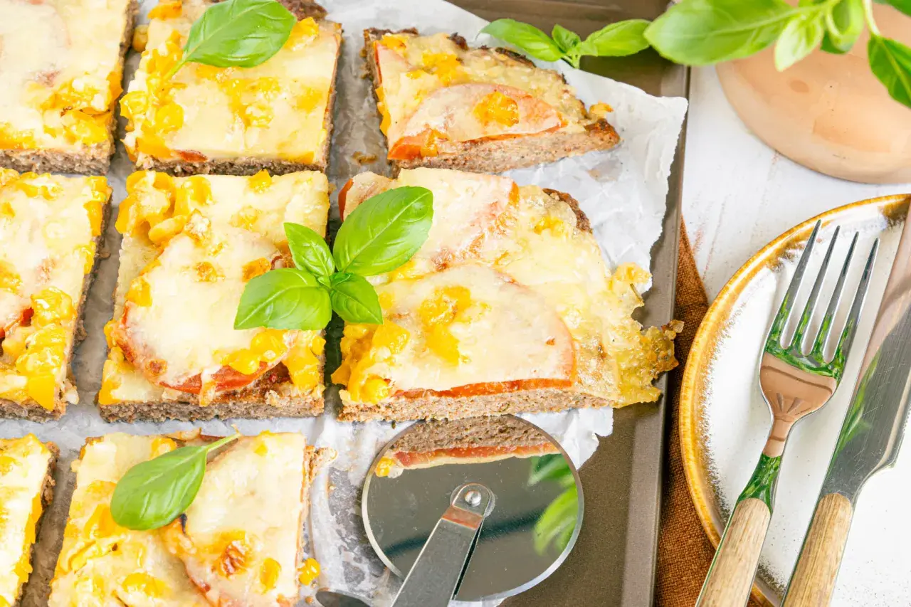 Herzhafte hackfleischpizza vom blech, Landfrauen-Art, mit Tomaten und Käse überbacken, garniert mit frischem Basilikum.