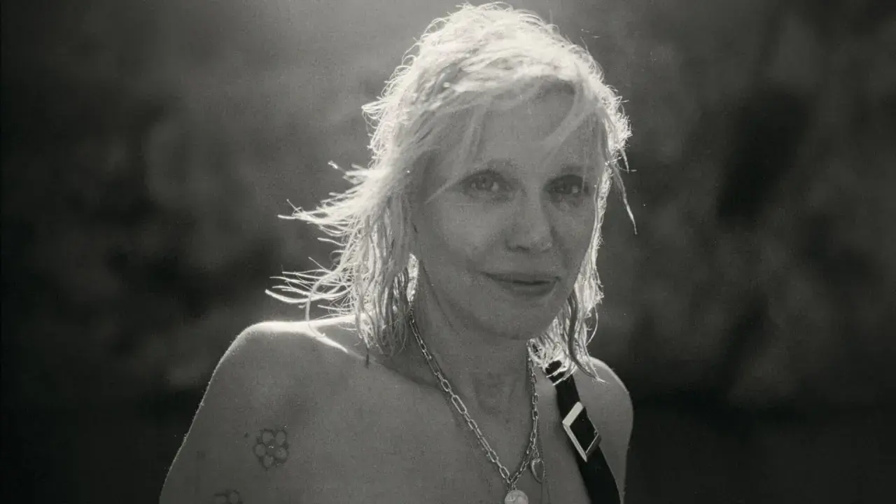 Courtney Love, ikona grunge, z rozwianymi włosami i tatuażem na ramieniu, emanuje siłą.