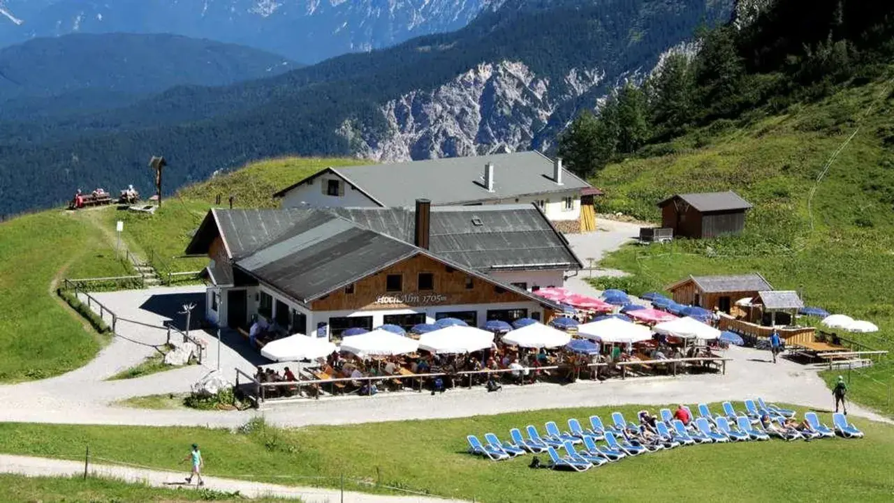 Die Hochalm Garmisch, ein beliebter Rastplatz mit vielen Gästen unter Sonnenschirmen, liegt malerisch vor einer beeindruckenden Bergkulisse.
