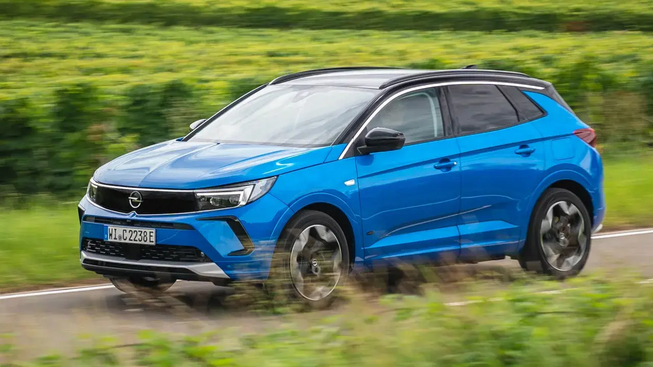 Blå Opel Grandland kör på en landsväg, omgiven av suddiga gröna fält. Kanske ett opel grandland problem med att hålla sig på vägen?