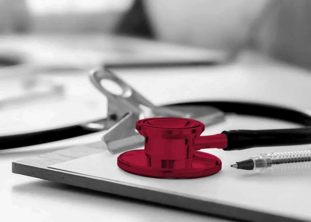 Un stéthoscope rouge vif sur un presse-papiers, prêt pour une visite médicale. Un stylo et une pince complètent la scène.
