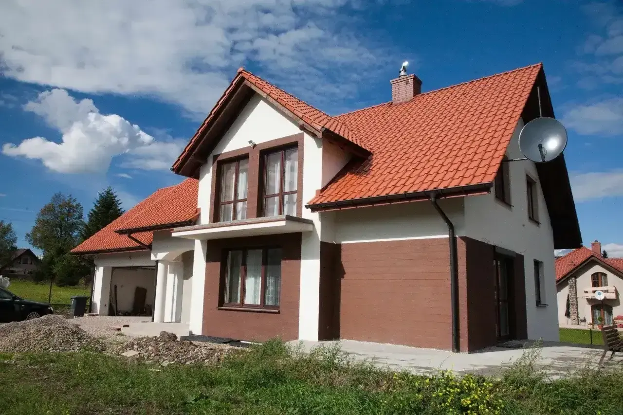 Nowy dom z białymi i brązowymi akcentami na elewacji zewnętrznej, z pomarańczowym dachem.