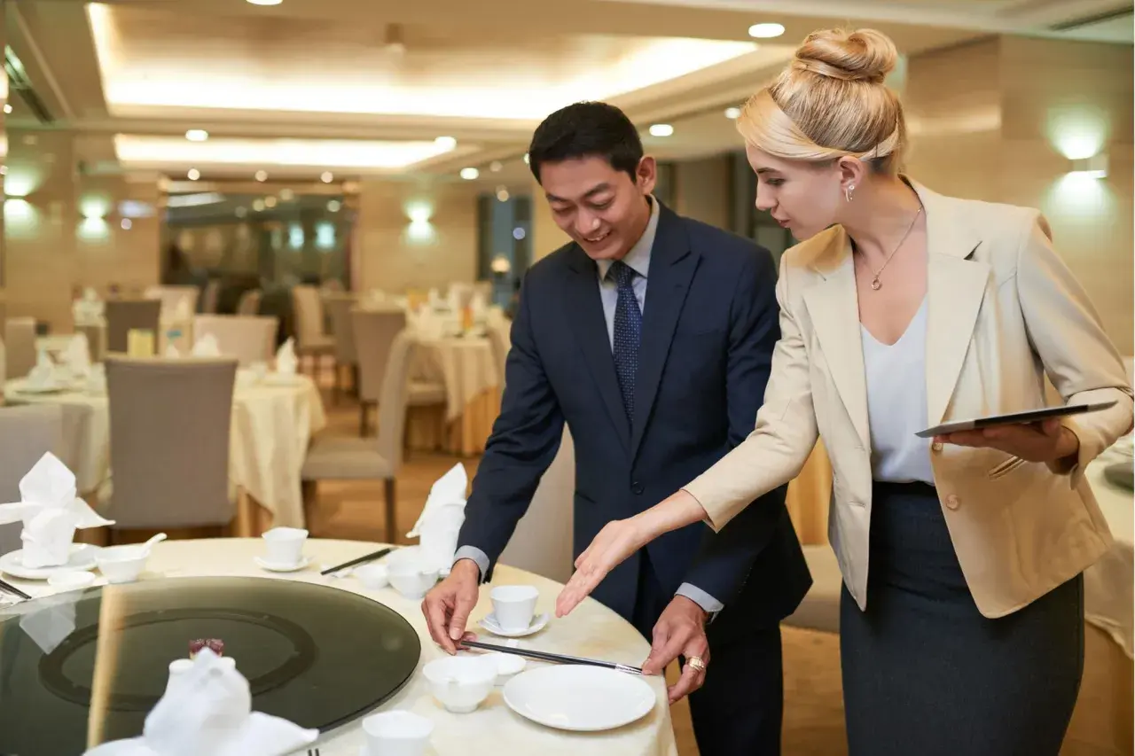 Ein Mann und eine Frau richten einen Tisch in einem Restaurant für ein Event her. Sie besprechen Details, die für das eventmanager gehalt wichtig sind.
