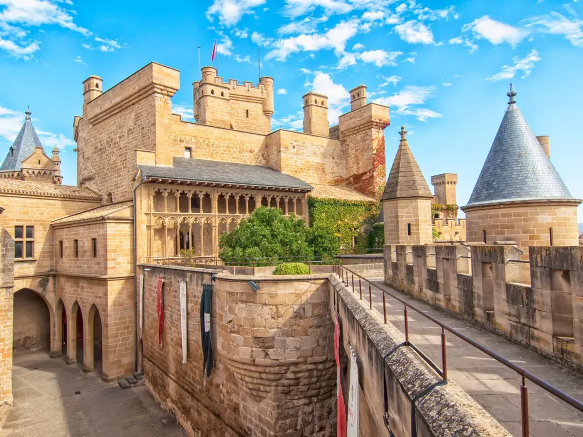 Imponente fortaleza de los castillos de España, con torres cónicas y un patio bajo un cielo azul y nubes blancas.
