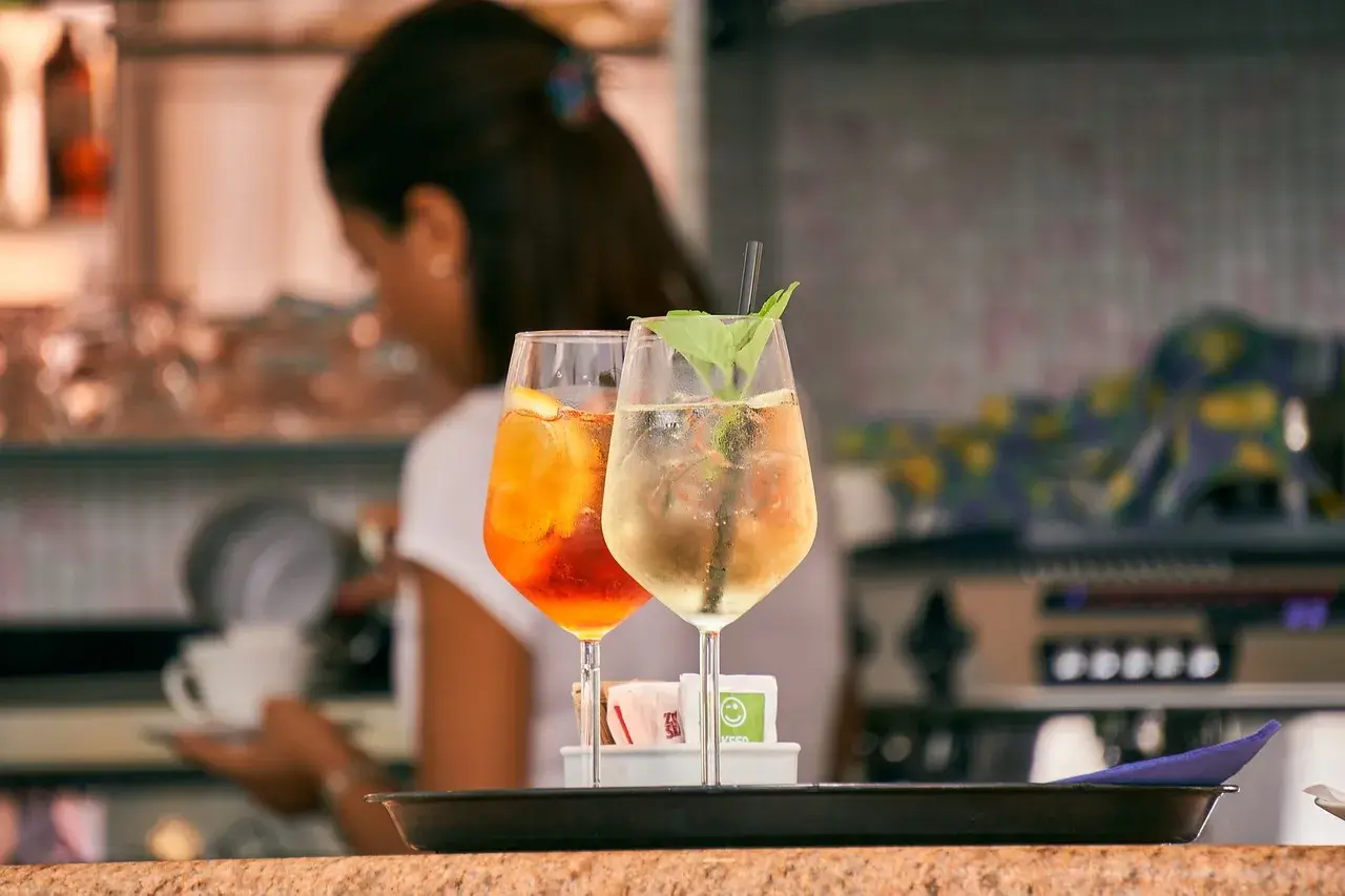 Dwa drinki: pomarańczowy Aperol Spritz i jasny Hugo. Różnica między aperol spritz a hugo w składnikach i kaloryczności jest widoczna.