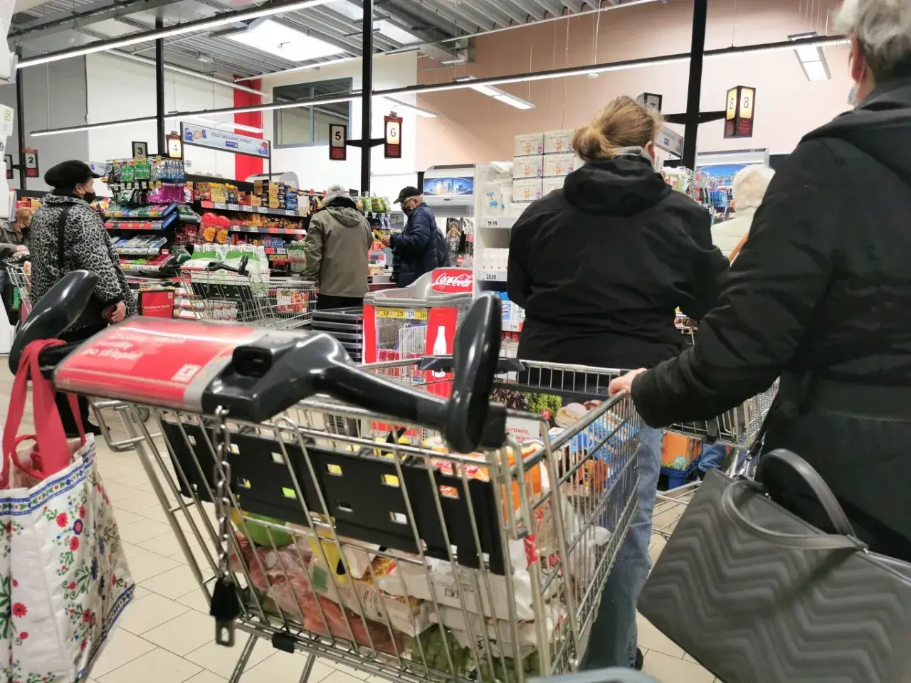 Ludzie robią zakupy w supermarkecie, zastanawiając się, czy w Wielką Sobotę można pracować. Wózek sklepowy pełen produktów.