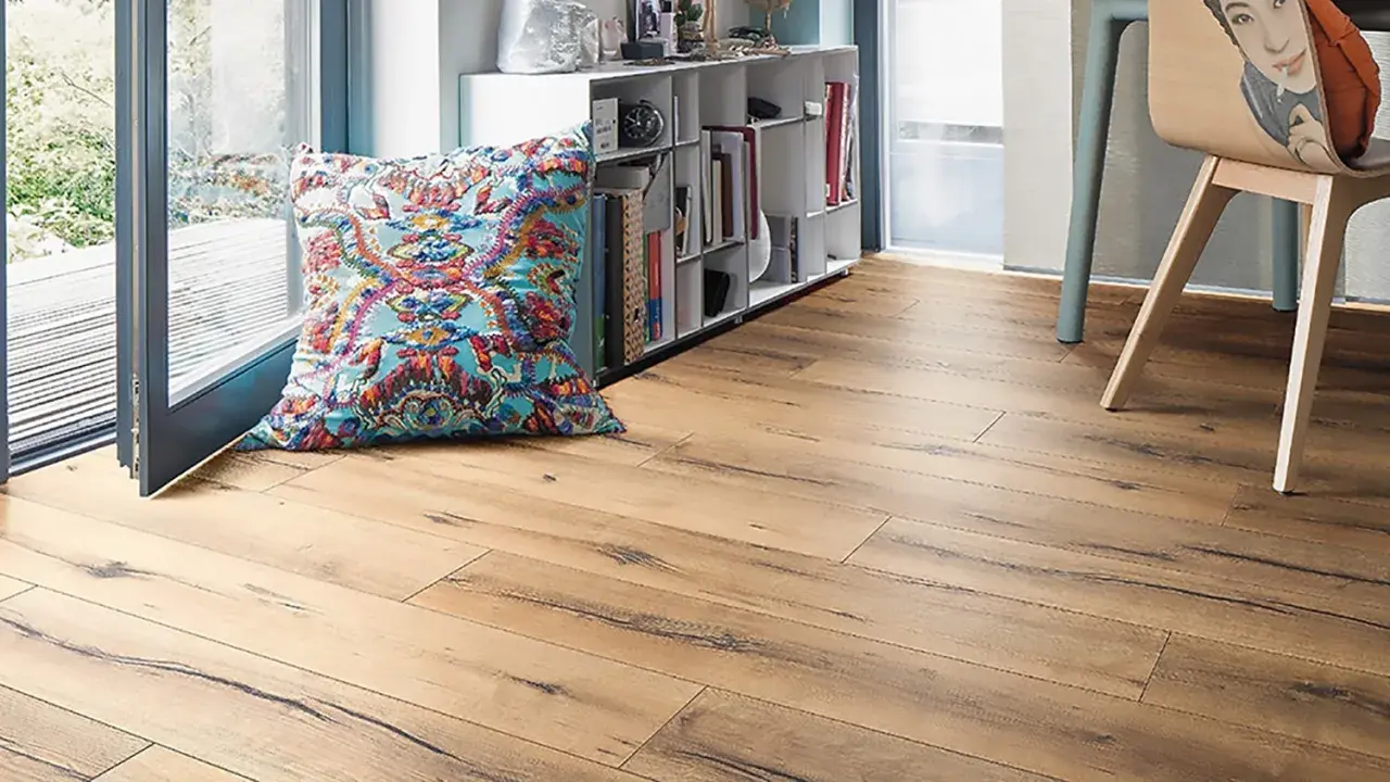 Un suelo laminado de madera clara con un cojín colorido y una estantería llena de libros.