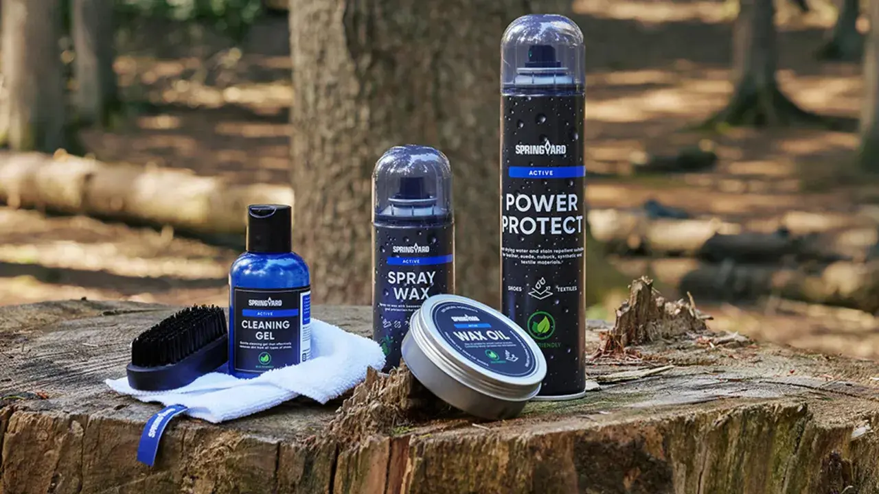 Produkter för impregnering av syntetskor: rengöringsgel, sprayvax, power protect och wax oil, placerade på en trädstubbe i skogen.