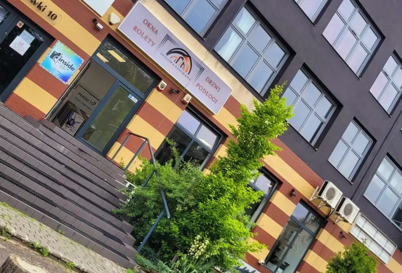 Elegancki budynek z oknami i drzwiami, z zielenią przed wejściem.