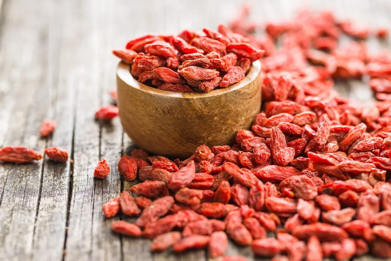 Suszone jagody goji rozsypane wokół drewnianej miseczki. Idealne do deserów, smoothie i jako zdrowa przekąska.