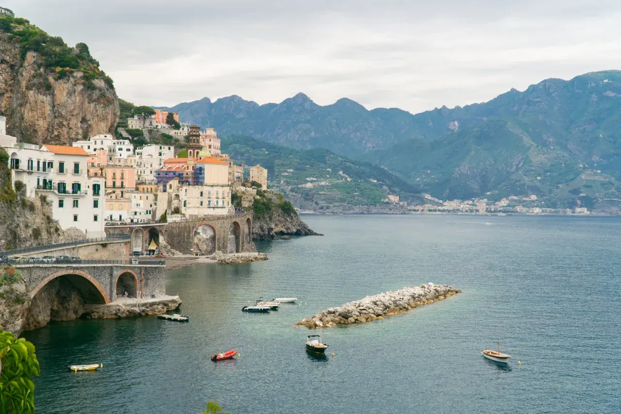 Malownicze miasteczko na klifie wzdłuż wybrzeża Amalfi, z łodziami na lazurowej wodzie i górami w tle.