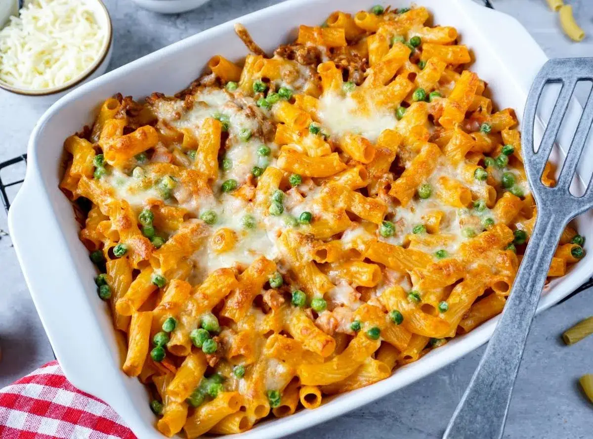 Herzhaftes Rigatoni al Forno mit Erbsen und geschmolzenem Käse in einer Auflaufform, bereit zum Servieren.