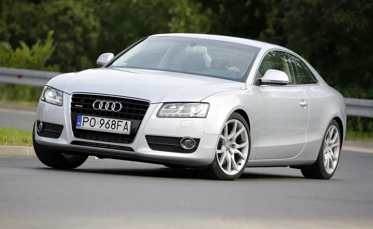 Srebrne Audi A5 z 2006 roku na drodze, z widocznym kierowcą.