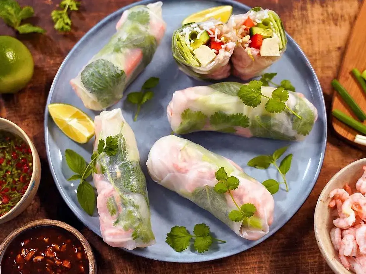 Färska sommarrullar med räkor och grönsaker, serverade med en smakrik vietnamesisk sås och limeklyftor.