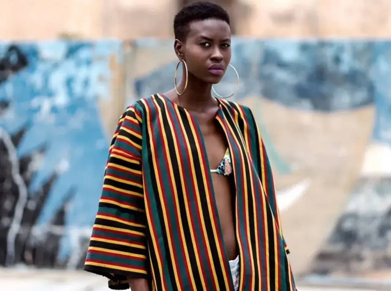 A woman models a vibrant Ankara fabric jacket with bold stripes of red, yellow, green, and black.