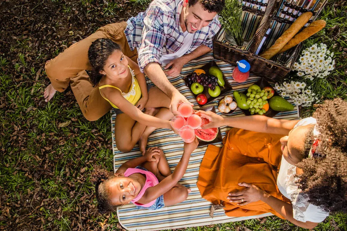 Familia disfrutando un picnic con frutas y bebidas. ¡Excelentes ideas picnic niños para un día soleado!