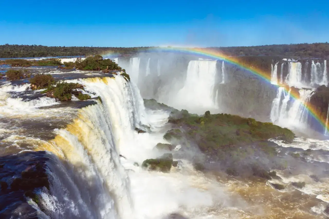 Potężny wodospad Iguazu, z tęczą unoszącą się nad mgłą wodną, otoczony bujną zielenią.