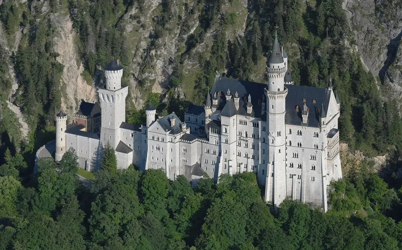 Bajkowy zamek w Niemczech, Neuschwanstein, wyrasta z zielonych lasów na tle skalistego zbocza.