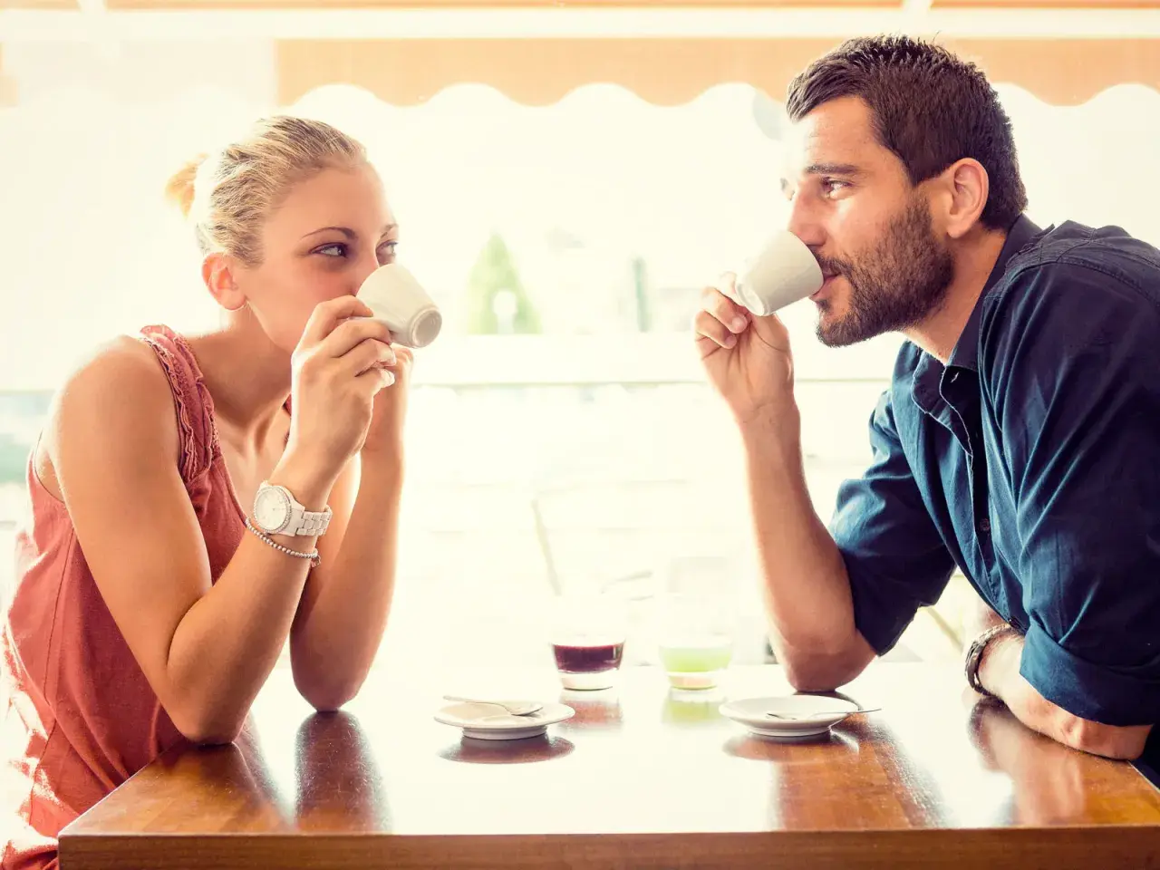 Coppia al bar, lui la guarda intensamente, un uomo innamorato in segreto che cerca il suo sguardo mentre bevono un caffè.