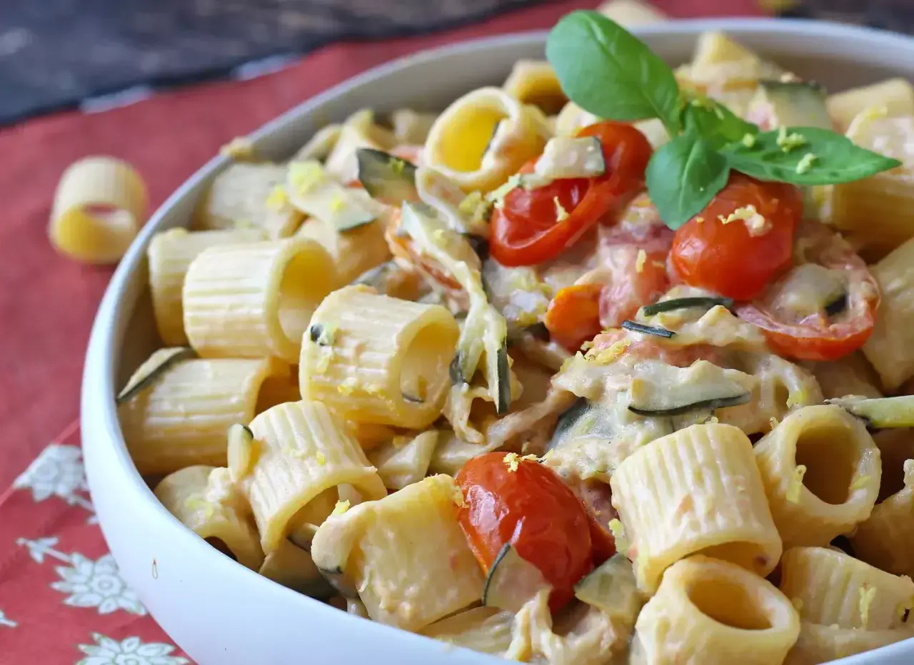 Piatto cremoso di pasta con zucchine, pomodorini e un tocco di Philadelphia, guarnito con basilico fresco.