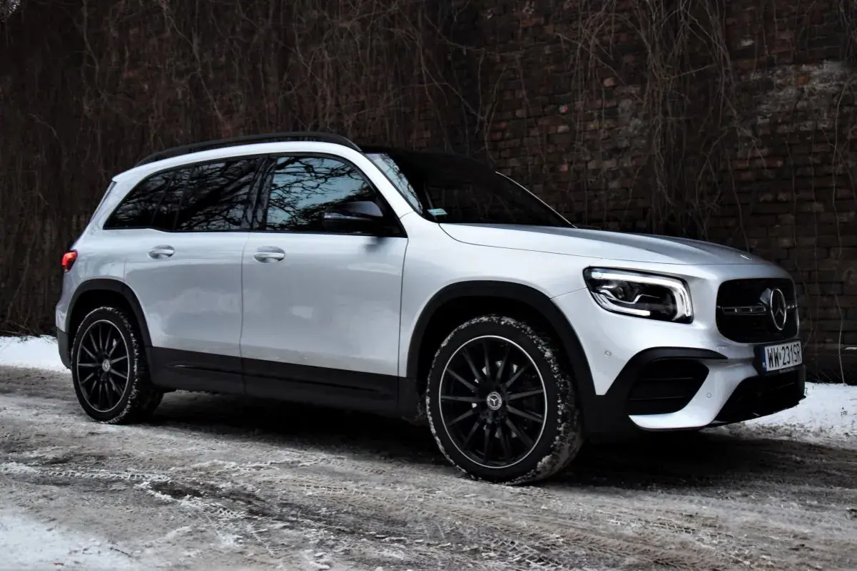 Srebrny Mercedes GLB 200 na zimowej drodze, z czarnymi felgami i przy ceglanym murze.