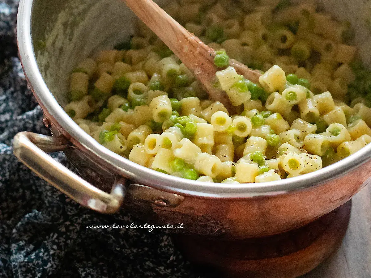 Un primo piatto cremoso di pasta e piselli, mescolata con un cucchiaio di legno in una pentola di rame.
