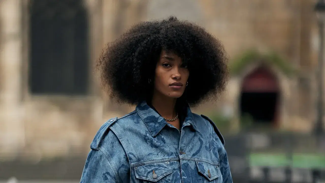 Frau mit Afro-Frisur trägt eine auffällige Jeansjacke, die perfekt zu einem lässigen Baggy Jeans Outfit passt.