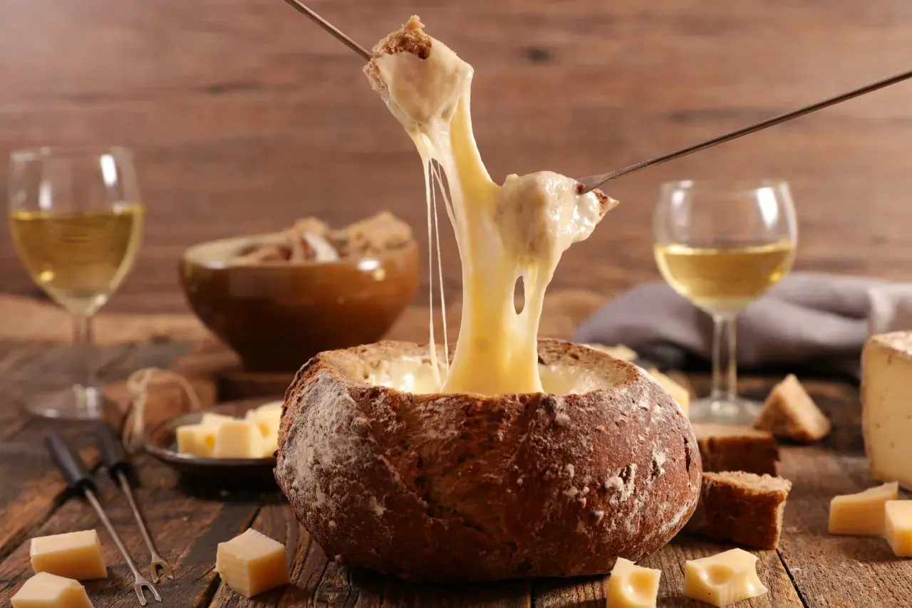 Un pain creusé sert de bol pour une fondue au vin blanc dégoulinante. Des morceaux de pain et de fromage sont prêts à être trempés.
