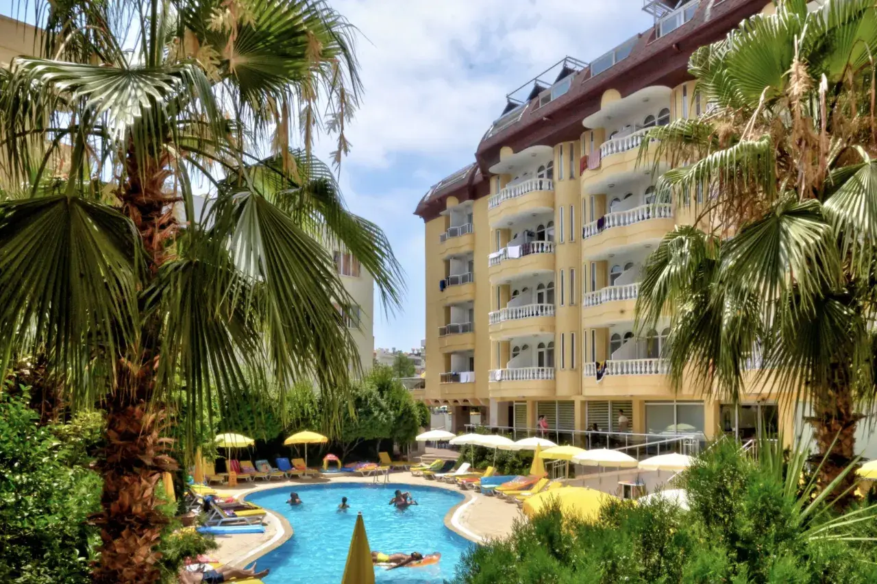 Basen z palmami i żółtym budynkiem hotelowym w tle.