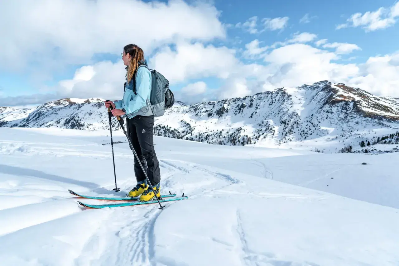 Frau mit Rucksack und Skitourenausrüstung in verschneiter Berglandschaft. Perfekte Packliste Skitour für Abenteuer.