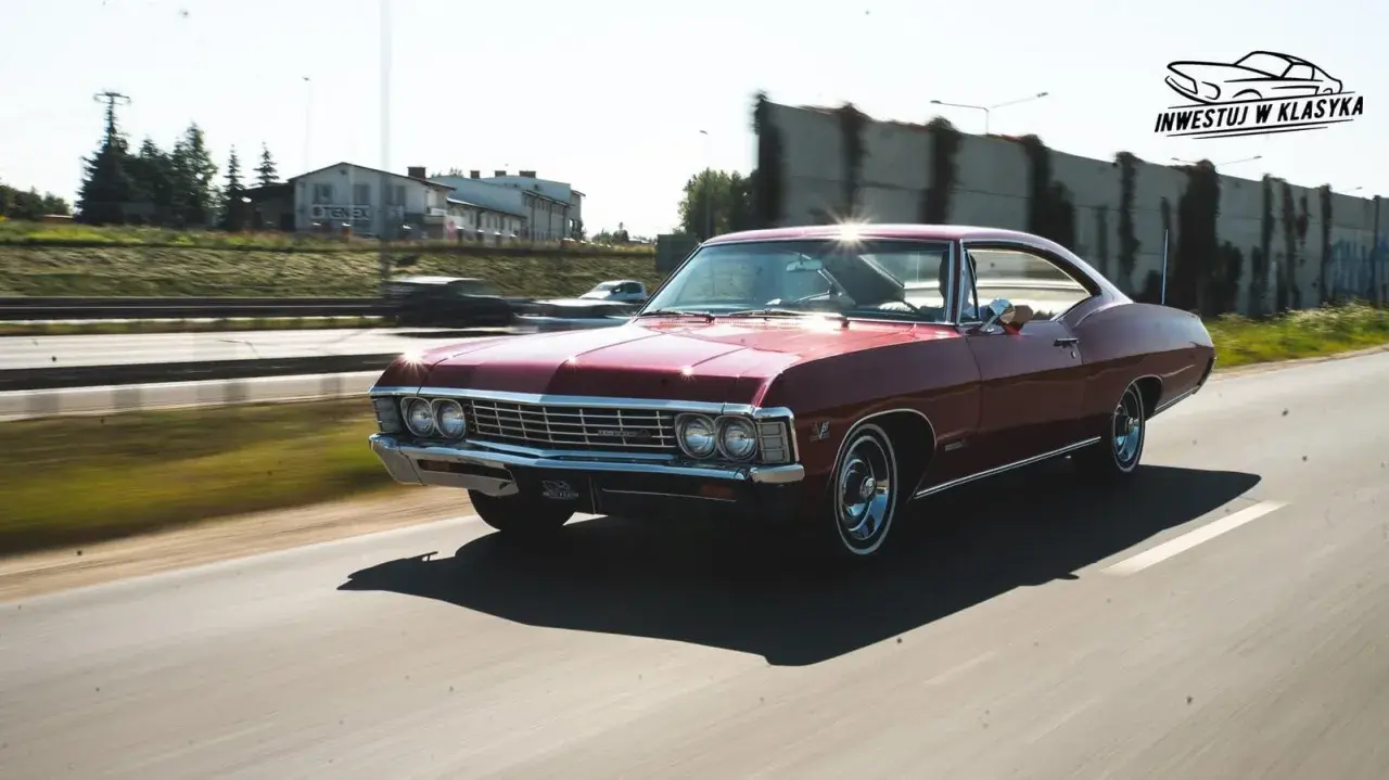 Czerwony Chevrolet Impala 1967 sunie po drodze, błyszcząc w słońcu. Klasyk w ruchu.