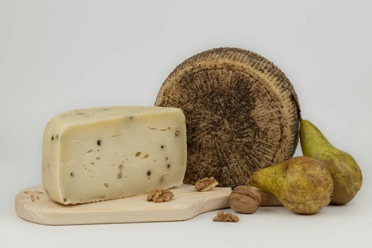 Varietà di tipi di pecorino, uno a spicchio con pepe nero, uno intero con crosta scura, pere e noci su tagliere di legno.