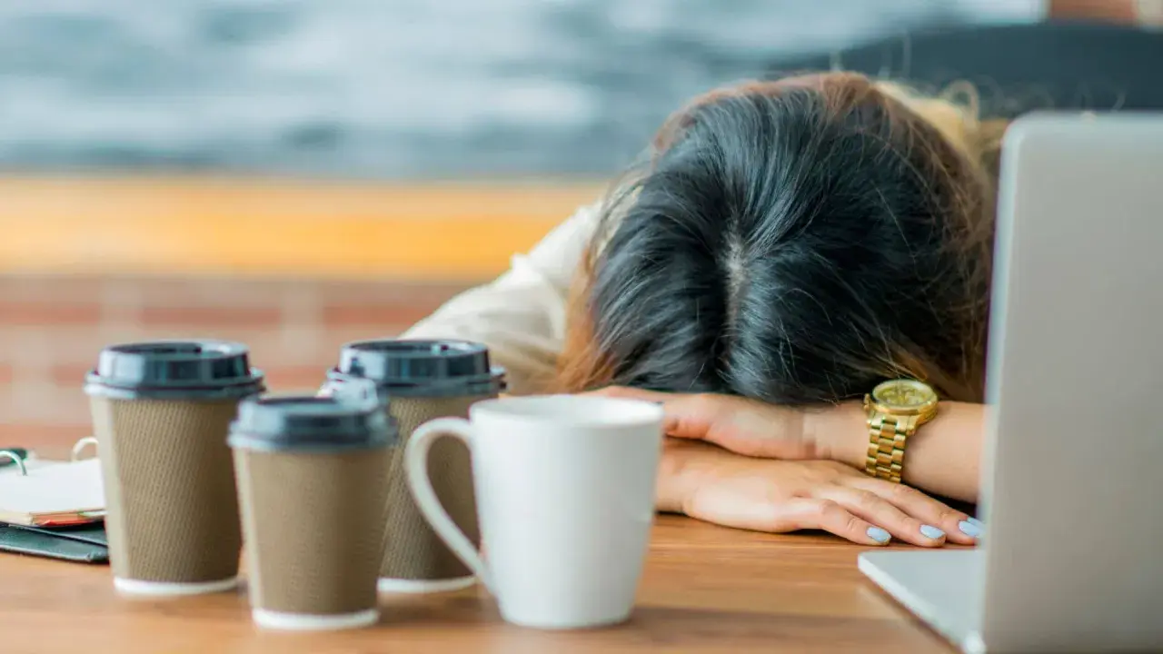 Erschöpfter Lehrer, Kopf auf dem Tisch, umgeben von Kaffeebechern. Die Anzeichen von **Lehrer Depression** sind deutlich.